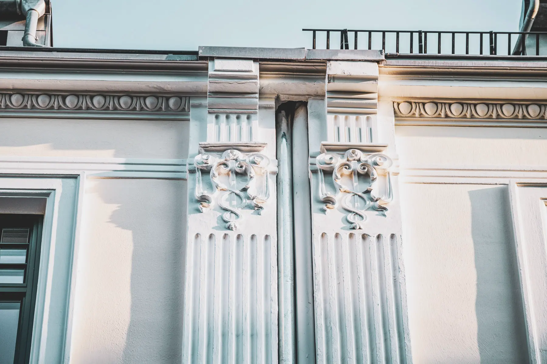 Zwei aufwendig gestaltete weiße Säulen mit Schmucktechnik am oberen Ende einer Hausfassade. Maler Juergens übernimmt mit handwerklichen Geschick und Präzision die Erarbeitung und Pflege der Schmuckverzierung.